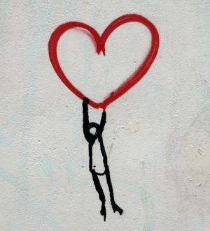 Stick figure hanging on to a floating heart